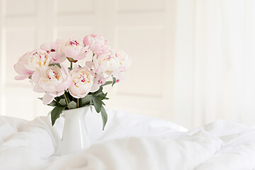 Bouquet of pink peonies on white bed linen. Modern interior in the bedroom. Wedding and festive style.
