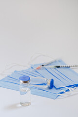 Creative ideas of vaccination concept. Top view of syringe with medical masks and vaccine vial glass bottles for vaccination against COVID-19. Coronavirus pandemic. Copy space. 