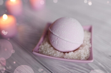 Pink bath bomb with sea salt in square bowl, pink candles on wooden gray bright bathroom table.