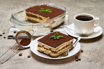 Traditional Italian Tiramisu dessert in glass baking dish and portion on grey concrete background