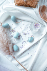 Light Blue easter eggs on a white background with lifestyle elements such as pampas grass, flowers and silk cloth