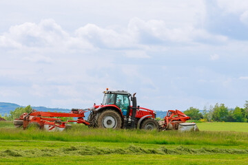 Big red tractor with two mowers mows the grass for silage