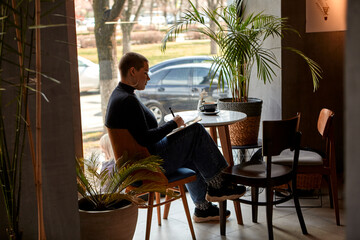 Young girl with short hair and nose piercing sits in a cafe and work at a tablet. The concept of freelancing and remote work.