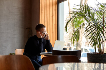 Young girl with short hair and nose piercing sits in a cafe. A woman is talking on the phone and work at a tablet. The concept of freelancing and remote work.