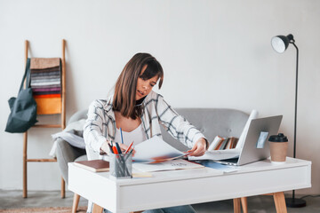 With laptop on the table. Young female freelance worker is indoors in home at daytime