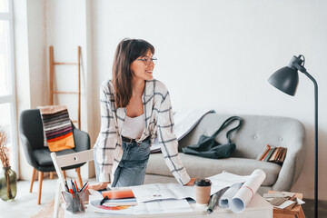 Standing near table. Young female freelance worker is indoors in home at daytime