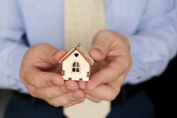 Real estate agent, wooden house in male hands. Man in office clothes with house model, purchase or rental home