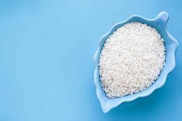 Uncooked white rice in a beautiful bowl. Blue background with copyspace. Concept of healthy eating