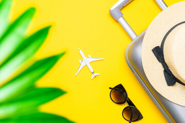 Suitcase, sunglasses with palm leaves and straw hat, white plane in travel composition on yellow background. Design of summer vacation holiday concept.