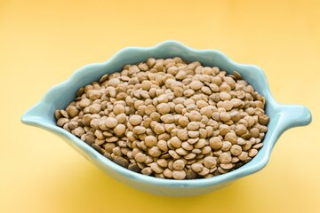 Organic green lentils in a beautiful bowl. Stock photo with yellow background. Concept of healthy eating, vegan diet and plant based protein