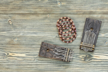 Two Kalimba Musical instruments with a dark wood base with a geometric pattern and an African female bracelet in the form of a spiral of seeds on an old wooden board
