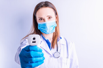 Fototapeta na wymiar Beautiful young doctor with mask gloves and stethoscope holding a laser thermometer in front point disease medicine concept