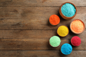 Colorful powder dyes on wooden background, flat lay with space for text. Holi festival