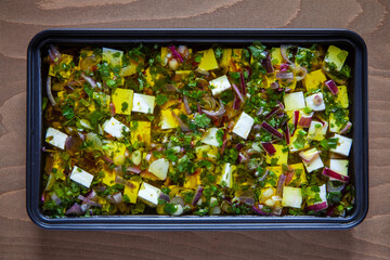Black tray with feta cheese marinated with olive oil, onion and herbs. Top view.