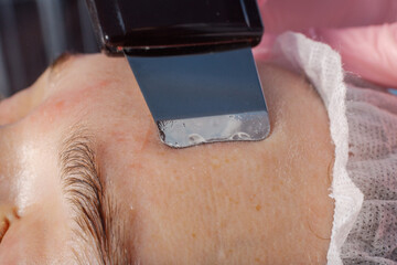 A professional cosmetologist performs an ultrasonic face cleaning procedure for a woman.