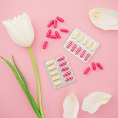 Medical composition with vitamins pills and white flowers on pink background. Flat lay