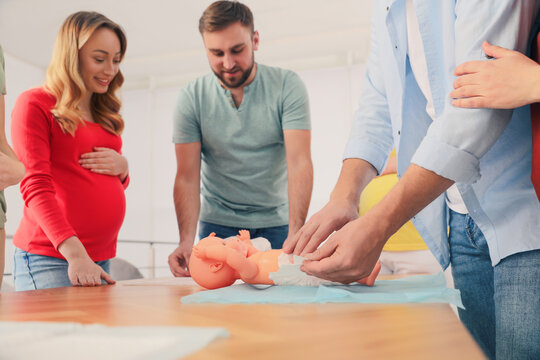 Future fathers and pregnant women learning how to swaddle baby at courses for expectant parents indoors, closeup