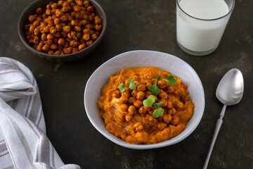 Thick pumpkin soup with baked chickpeas and radish sprouts in a plate with a glass of milk on the table, delicious healthy dinner