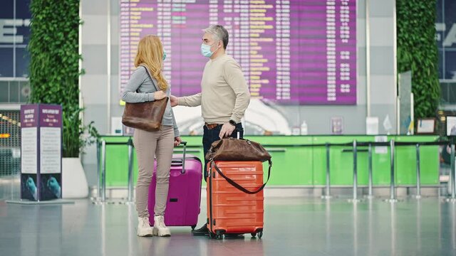 Middle aged man and woman travellers standing near flight board at airport, going to departure