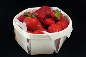 Fraises gariguette dans une barquette en bois en gros plan sur fond noir