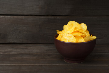 Potato chips in brown plate on dark wood background