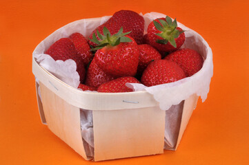 Fraises gariguette dans une barquette en bois en gros plan sur fond orange