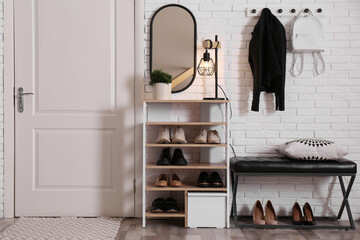 Fototapeta na wymiar Shelving unit with shoes and different accessories near white brick wall in hall. Storage idea