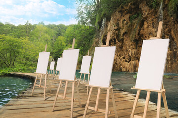 Wooden easels with blank canvases near river on sunny day