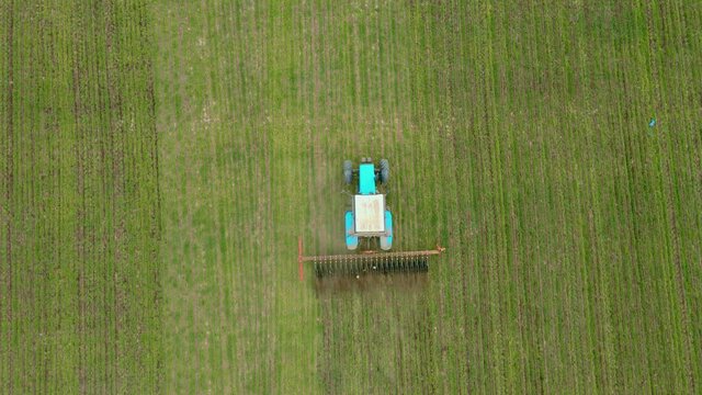 Top down view on agronomic tractor with rotary harrow plowing crops for better growing wheat or barley and better oxygen permeability to soil. Concept of work in agricultural farm for making business