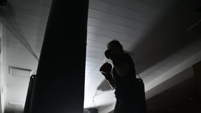 dark silhouette of a boxer girl practicing punches on a boxing bag.