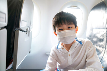 Fototapeta na wymiar Asia boy wear face mask on the airplane and sit beside windows. Coronavirus disease pandemic outbreak impact to business airline. Travel during COVID 19 pandemic. New normal lifestyle