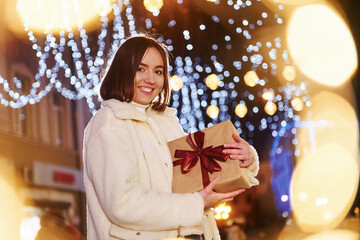 Pretty young woman with gift box standing outdoors on the street