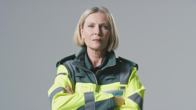 Serious mature female paramedic wearing uniform in front of plain studio background - shot in slow motion
