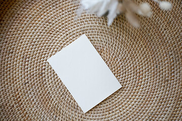 Summer stationery still life. Closeup of blank card mock-up with dry leaf in boho interior. Grunge beige concrete background. Flat lay. Moody boho design