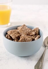 A bowl of wholemeal bran cereal and glass of orange juice on a breakfast table