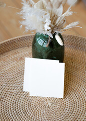 Summer stationery still life. Closeup of blank card mock-up with dry leaf in boho interior. Grunge beige concrete background. Flat lay. Moody boho design
