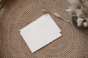 Summer stationery still life. Closeup of blank card mock-up with dry leaf in boho interior. Grunge beige concrete background. Flat lay. Moody boho design