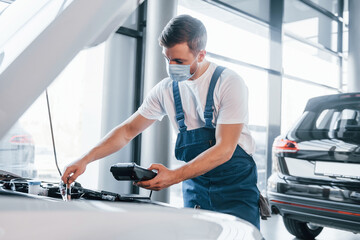 Young man in white shirt and blue uniform repairs automobile