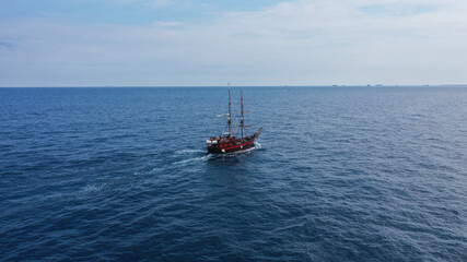 Aerial view of a big sailboat sailing on the wavy ocean under the cloudy blue sky