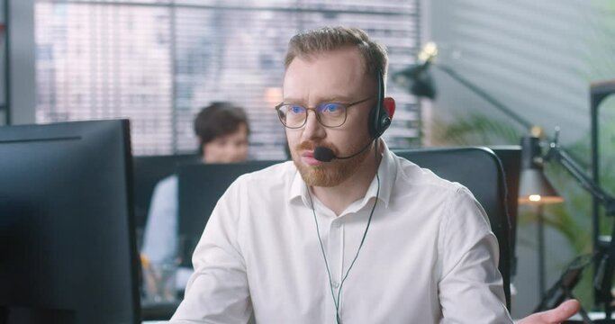 Adult man with glasses works in support service and sitting in office nervously talking to client. Call center concept.
