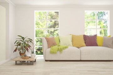 Fototapeta premium White living room with sofa and summer landscape in window. Scandinavian interior design. 3D illustration