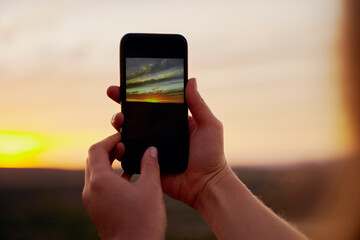 Closeup of hands of young male hiker clicking beautiful morning sunrise on smartphone