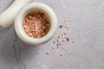 Large pink himalayan salt in a mortar for seasoning on a marble background, top view
