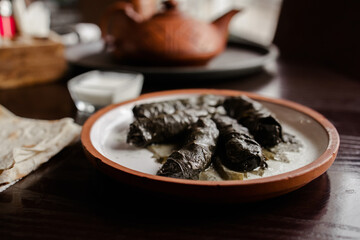 Georgian dish dolma. minced meat in grape leaves on a clay plate with white sauce