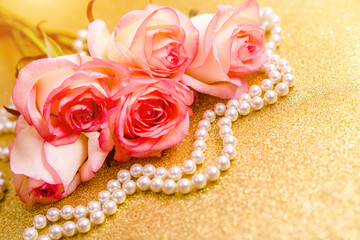 Pink rose and pearl necklace on a shiny gold background