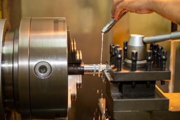 The hand of machine operator setting the coolant tube on late machine. The operation of lathe machine cutting the metal shaft with lubricant cooling method.