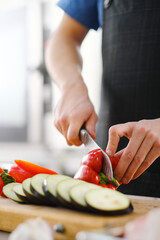 The male Caucasian chef cuts vegetables, peppers, tomatoes and eggplants on a wooden cutting board.