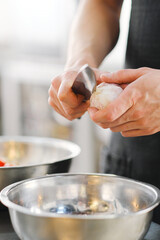 The male chef cleans and cuts the garlic with a knife on a wooden cutting board close-up.