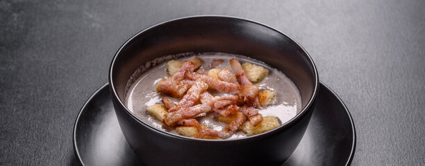 Fresh delicious hot puree soup with mushrooms and bacon in a black plate