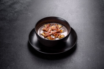 Fresh delicious hot puree soup with mushrooms and bacon in a black plate